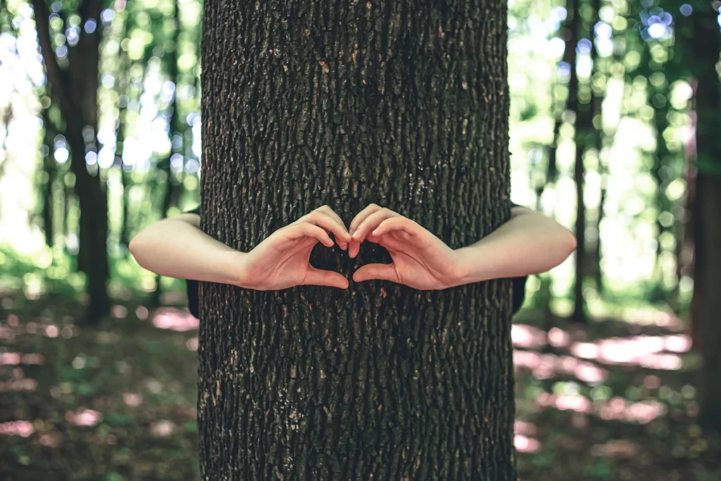 Femme enlace un arbre et fait le symbole du coeur. 